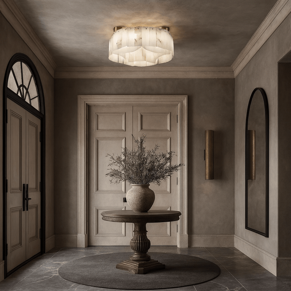 A round wooden table with a large vase of greenery sits on a circular rug in an elegant beige entryway with double doors, arched mirrors, and the Milton Marble Flush Mount by Morsale.com lighting the space overhead.