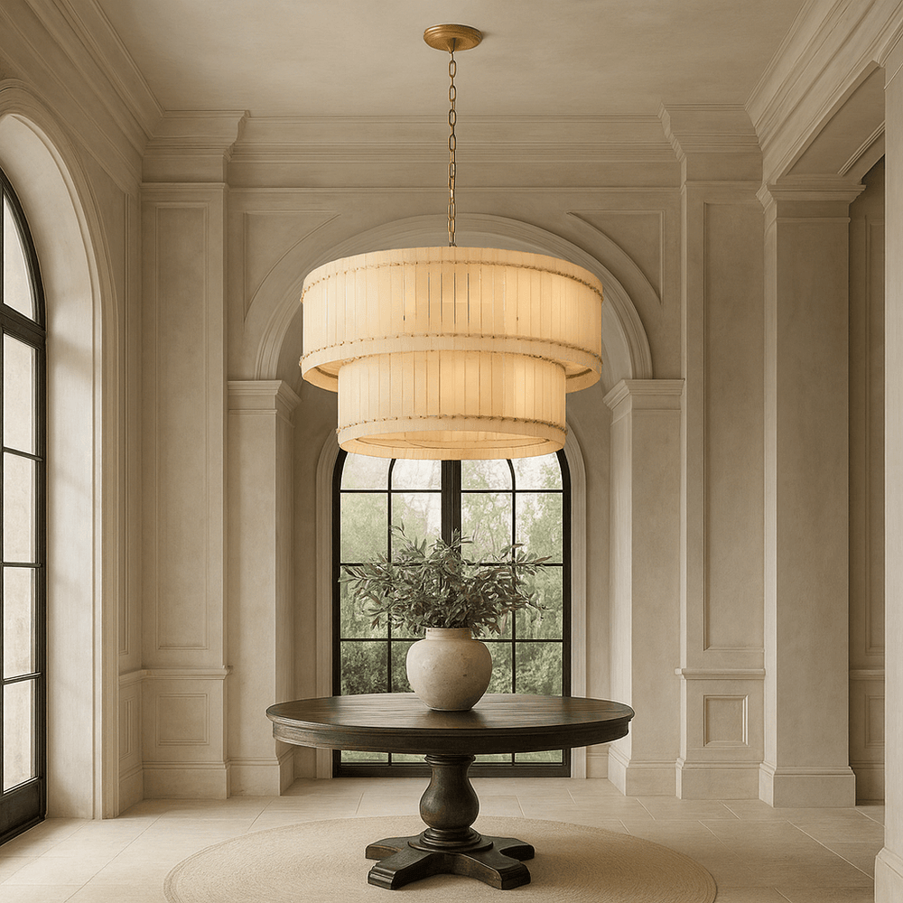 A round wooden table with a potted plant sits on a rug beneath the Morsale Valmont 2-Tier Marble Chandelier 39" in an elegant, neutral-toned room with tall arched windows and detailed wall paneling.