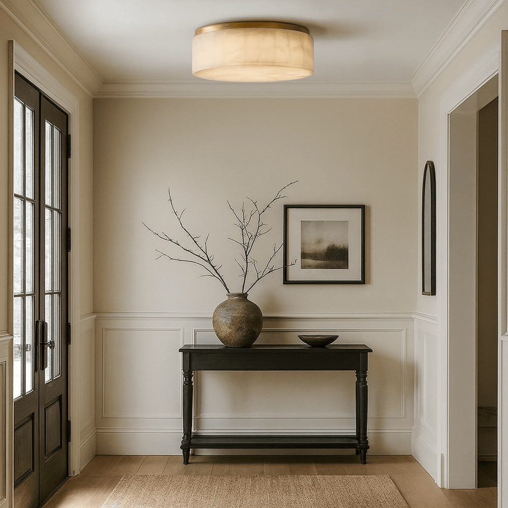 
                  
                    A minimal entryway features a black console table, a large ceramic vase with bare branches, a small bowl, framed art on the wall, and the Milton Marble Flush Mount by Morsale.com. Neutral tones create an elegant atmosphere.
                  
                