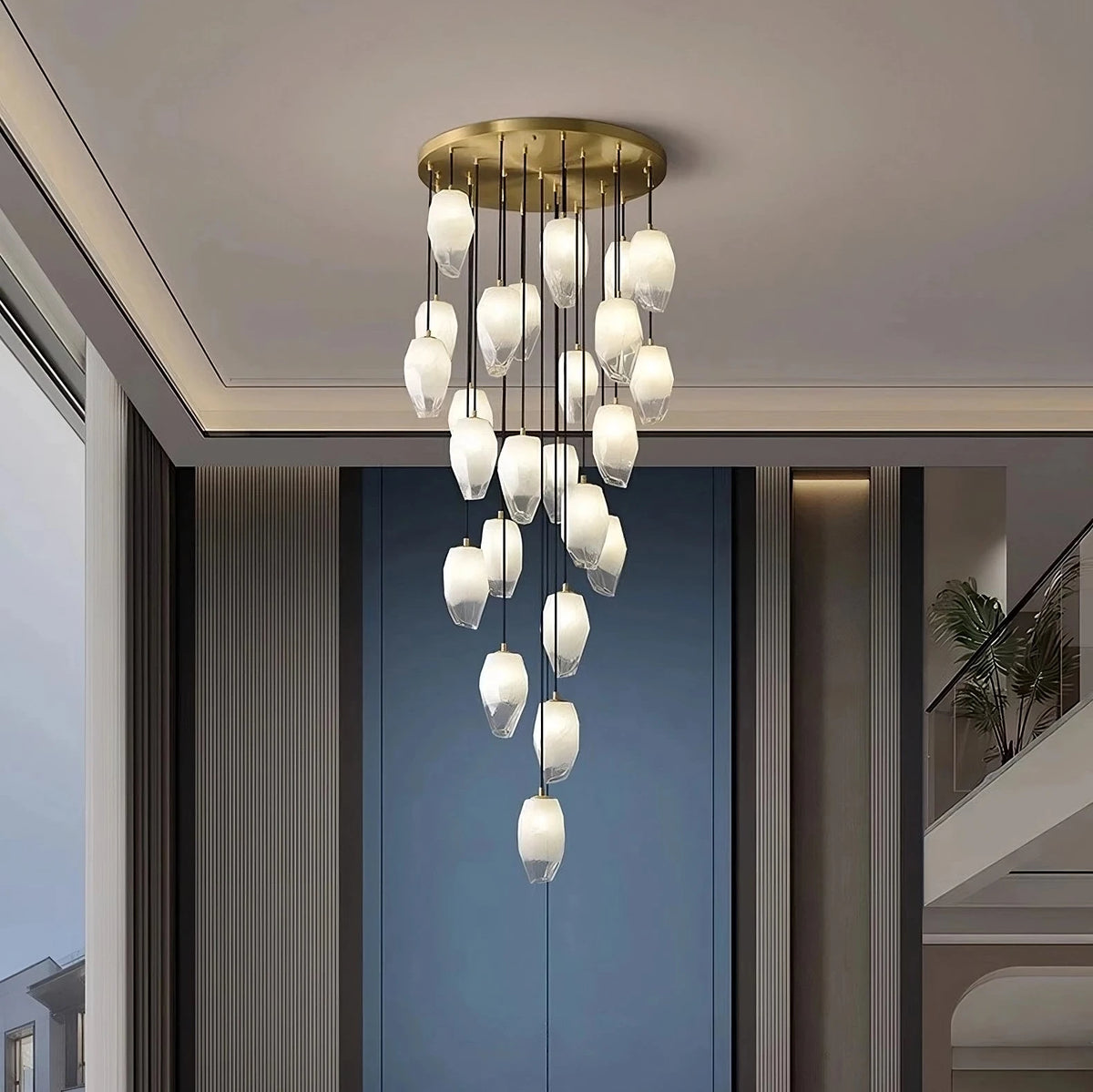 The Frost Glass Pendant Foyer Chandelier by Morsale.com is showcased, featuring multiple hanging teardrop-shaped white glass bulbs that create a cascading effect. This dimmable LED light fixture, boasting a minimalist design, is installed in a room with high ceilings, and a large window on the left offers an outdoor view.