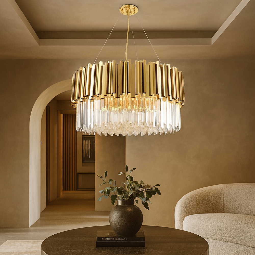 The Gio Gold Plated Crystal Chandelier by Morsale.com hangs in a beige-toned living room with a round table, greenery-filled vase, and curved sofa, adding elegant modern lighting to the space.