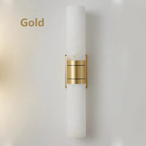 A modern Natural Marble Indoor Wall Sconce Light by Morsale.com with a sleek white cylindrical shade and a central gold metallic band is mounted on a white wall. Incorporating natural marble, this indoor sconce exudes a minimalist and elegant design. The word "Gold" is displayed on the left side of the image.