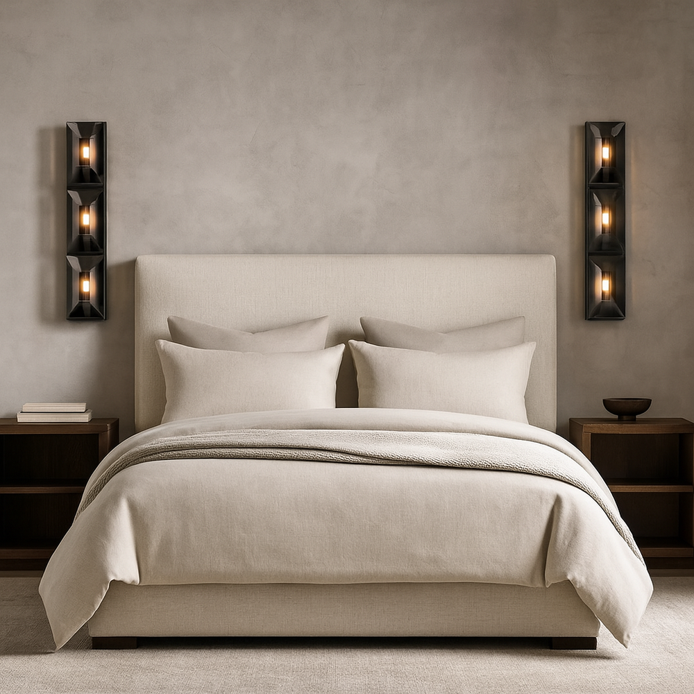 A modern, minimalist bedroom featuring a beige upholstered bed with matching bedding, two wooden nightstands, and Brookhill Crystal Wall Sconces by Morsale.com with exposed bulbs mounted on each side of the bed.