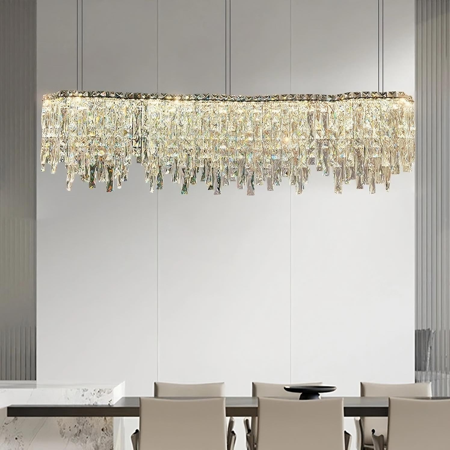 The Morsale.com Bacci Crystal Modern Dining Room Light Fixture 47" elegantly hangs from the ceiling above a contemporary dining table set with six beige chairs. This dimmable LED chandelier adds versatility to the minimalist decor, which features light gray walls and vertical grooves that enhance the sophisticated ambiance.