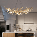 A modern kitchen with a marble backsplash, stainless steel refrigerator, wooden island with two bar stools, and the Bigman Albero Copper & Crystal Chandelier—a striking fixture shaped like tree branches adorned with crystals.