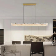 Modern kitchen with a luxurious design featuring a marble island, transparent bar stools, and the Morsale 60" Natural Marble Dining Room Light Fixture elegantly hanging above. The backsplash showcases a marble texture, while the sleek cabinets enhance the minimalist aesthetic.