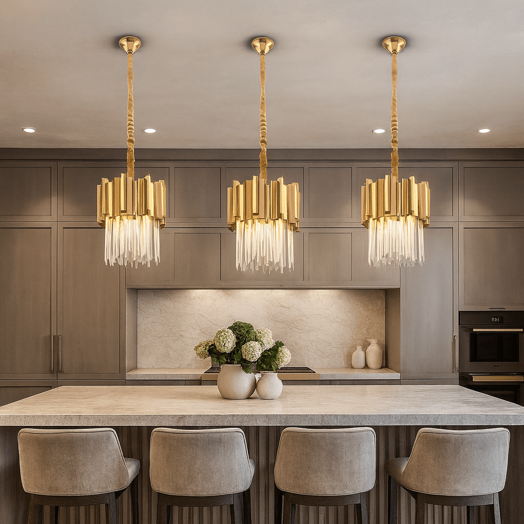 A modern kitchen features a large island illuminated by the Gio Crystal & Gold Pendant from Morsale.com, four upholstered bar stools, taupe cabinetry, built-in appliances, and a vase of white hydrangeas as a centerpiece.