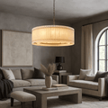 A modern living room with neutral tones features a Morsale Valmont Marble Round Chandelier 39", beige sofas, a square coffee table with dried grass in a vase, wall art, a black table lamp, and an arched window with beige curtains.