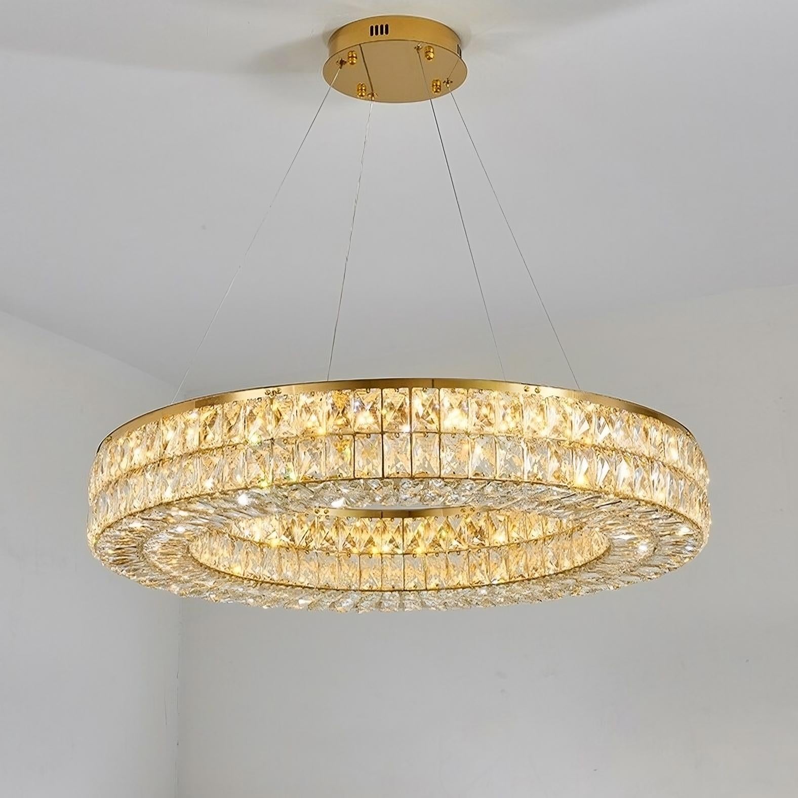 A Bacci Crystal Modern Chandelier, Gold from Morsale.com with a gold electroplated frame and two concentric circular tiers adorned with crystal accents, suspended from the ceiling by thin wires. The crystals capture and reflect light, creating an elegant and luxurious ambiance in the room.