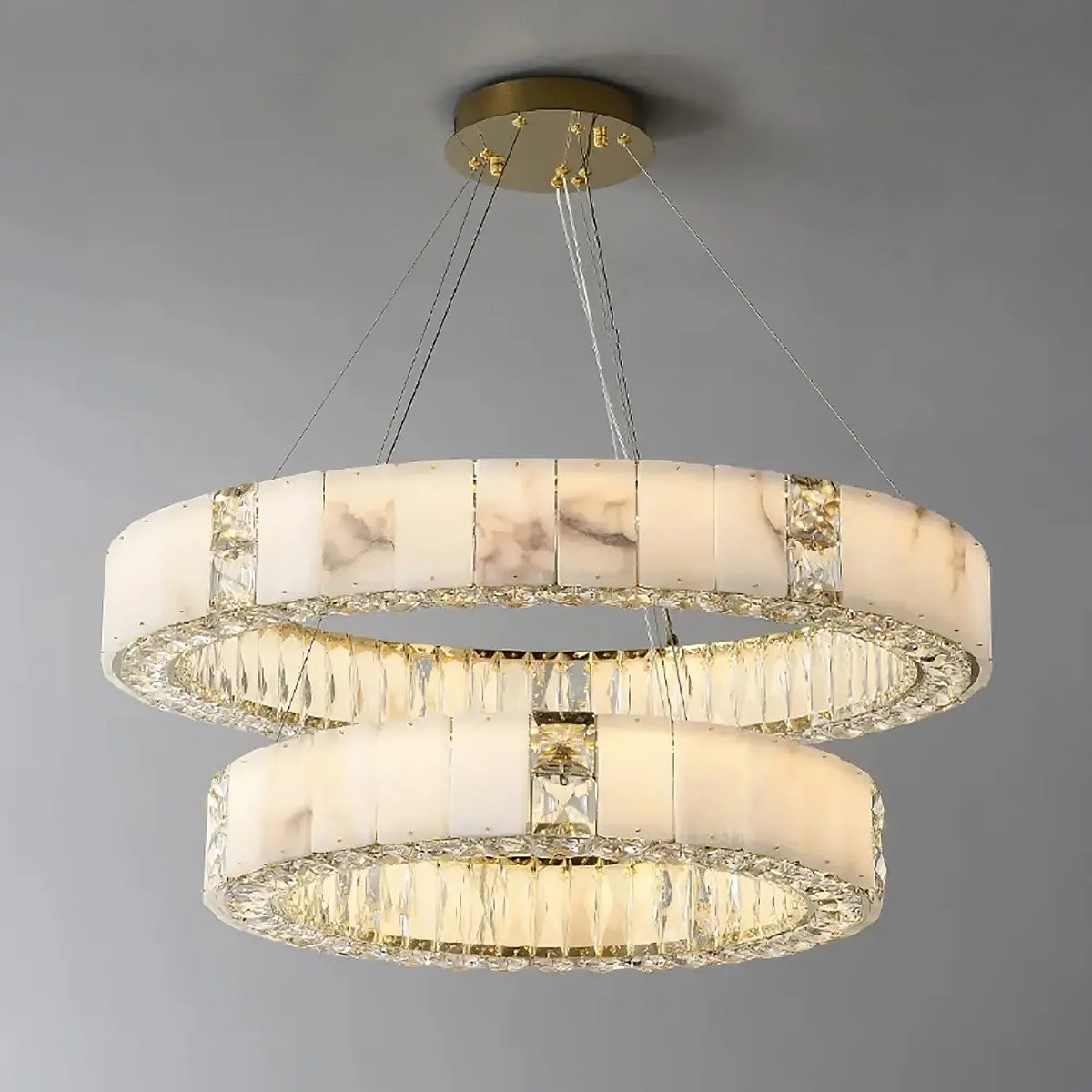 A Natural Marble & Crystal Modern Ceiling Light Fixture from Morsale.com, with two circular LED rings, adorned with a combination of opaque white and clear crystal-like segments, suspended by thin cables from a round, gold-toned base. The rings are stacked vertically, creating an elegant layered effect that complements any luxury home décor.