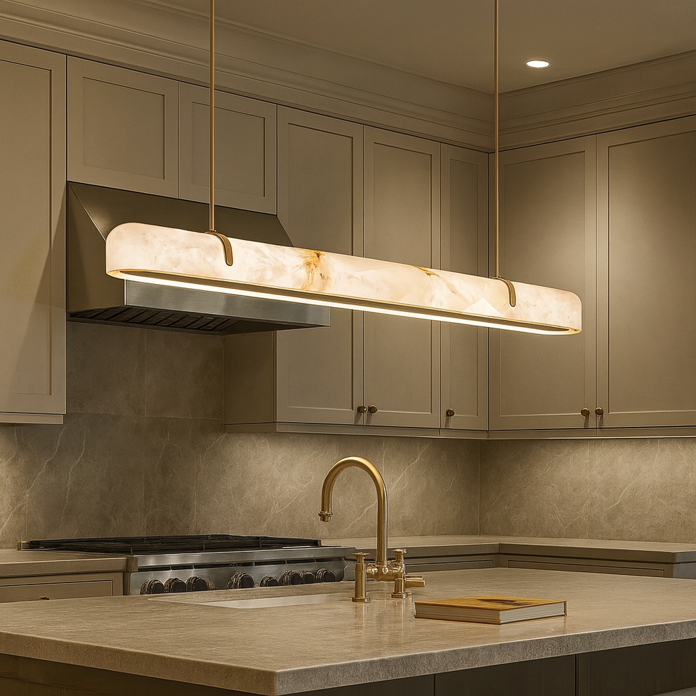 Modern kitchen with beige cabinets, marble backsplash, gold faucet, and the Windsor Marble & Copper Linear Pendant by Morsale illuminating the central island where a closed book rests. The space feels warm and elegant.