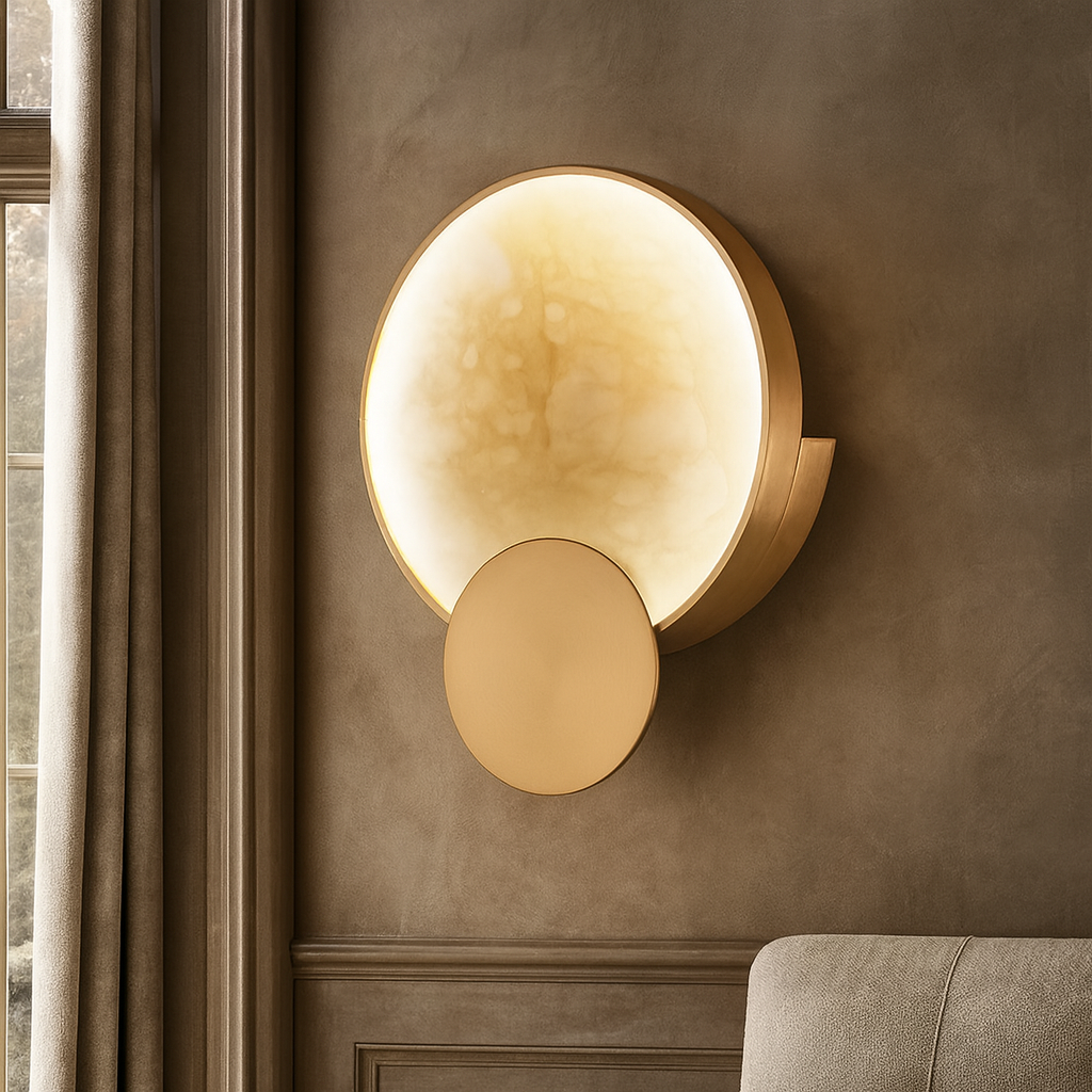 The Barley Marble Sconce by Morsale.com, featuring a large glowing circular light above a smaller gold disk, is mounted on a taupe wall near a window with beige curtains and a glimpse of a light-toned sofa.