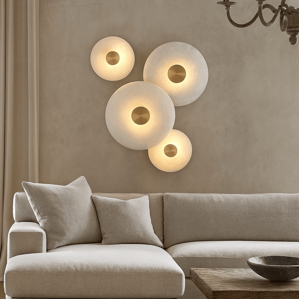 
                  
                    A modern living room features a light beige sofa, cozy cushions, a wooden table, and four Morsale.com Solena Marble Disc Wall Sconces of varying sizes softly glowing on a neutral-toned wall.
                  
                