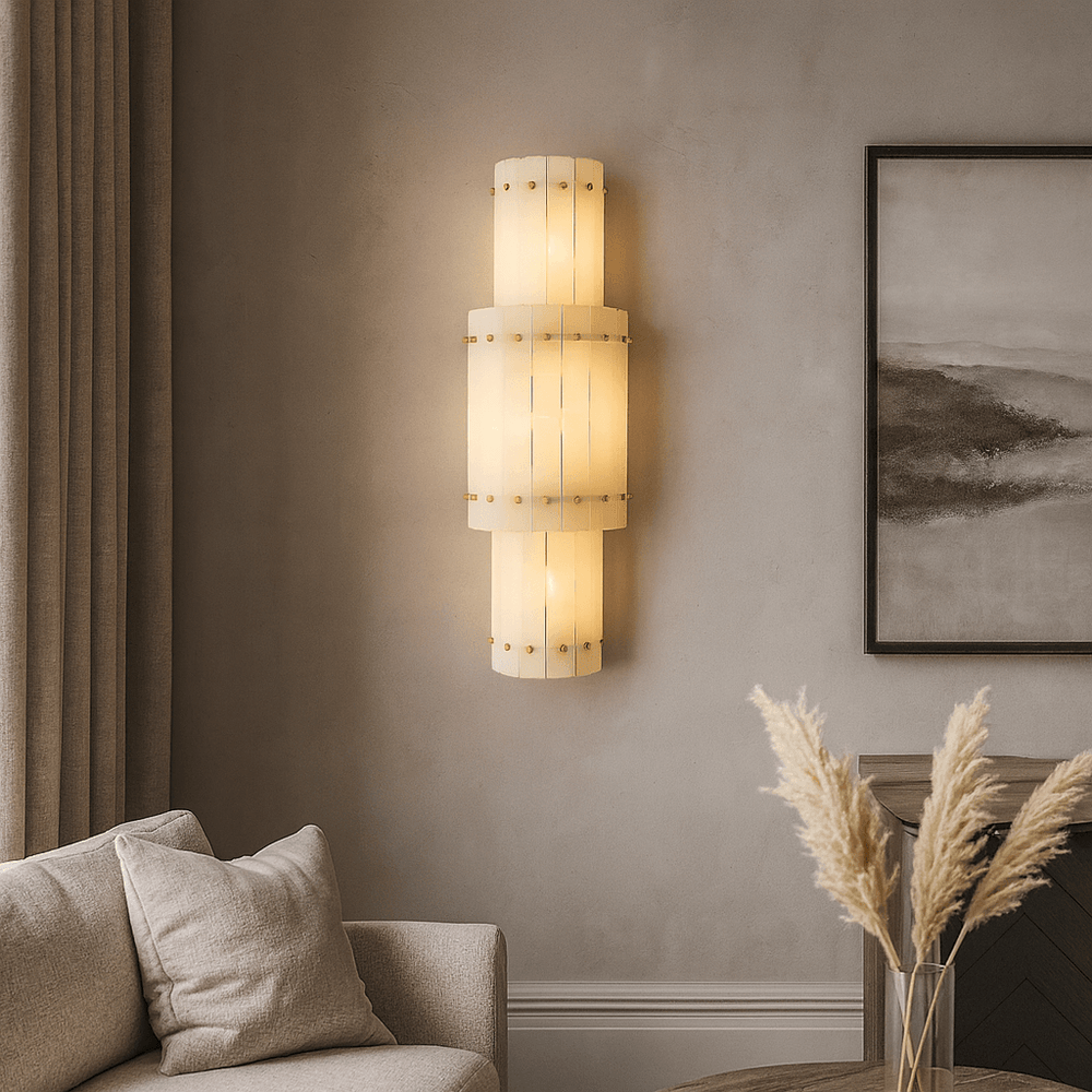 The Valmont Marble Wall Sconce by Morsale casts a warm glow in a neutral living room with a beige sofa, taupe curtains, abstract artwork, and a vase of dried pampas grass.