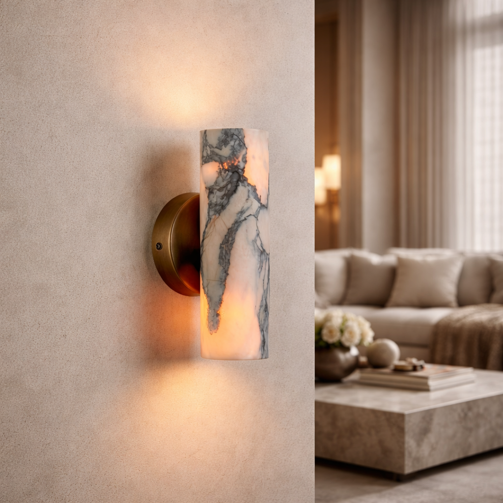 The Moonshade™ Marble Wall Sconce by Morsale.com casts warm light from its marbled cylindrical shade, enhancing a stylish living room with a beige sofa, coffee table, and large windows in the background.