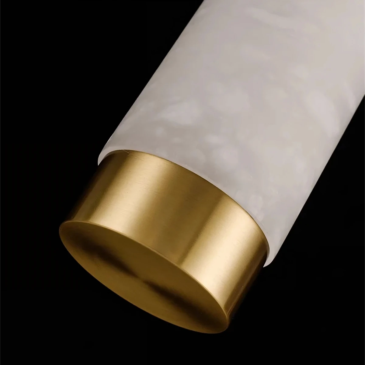 Close-up shot of a cylindrical object against a black background. The object has a white marbled texture and is capped with a gold-colored base. The sleek, modern design suggests it could be the 23" Natural Marble Pendant Light from Morsale.com, featuring dimmable LED functionality that blends style and utility seamlessly.