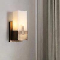 The Morsale Natural Marble Wall Lamp features a modern design with a white frosted glass shade and brushed metal base, mounted on a light wall beside beige curtains—ideal for those seeking sleek, stylish wall lighting.