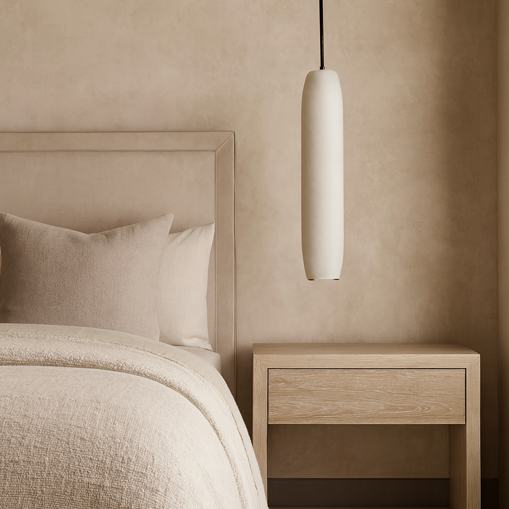
                  
                    Minimalist bedroom with a beige upholstered bed, textured bedding, wooden nightstand, and the Moonshade Marble Pendant by Morsale.com—a modern cylindrical white light—hanging above the table. The color palette is soft and neutral.
                  
                