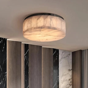 Introducing the Moonshade Natural Marble Ceiling Light Fixture from Morsale.com: a modern lighting solution featuring a round, semi-translucent shade and energy-efficient LED lights that emit a warm glow. The background showcases a contemporary wall design with vertical wooden panels and sections of black and white marble.