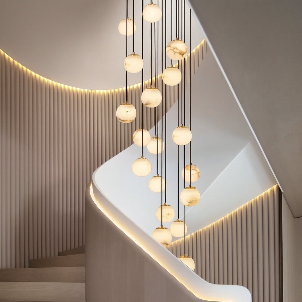 Modern staircase with a curved white railing, vertical wall panels, and multiple Brighton Marble Ball Chandeliers by Morsale with LED bulbs at varying heights, all lit by warm recessed wall lighting.