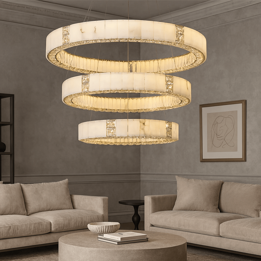 Three Aurelia Marble & Crystal Chandeliers from Morsale.com hang above a round coffee table, surrounded by beige sofas in a stylish, minimalist living room accented with abstract wall art and luxurious lighting.