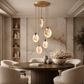 Luxury RH-style dining room with round dark wood table and upholstered chairs, featuring a modern marble chandelier with brass rods suspended above the table.