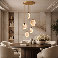 Luxury RH-style dining room with round dark wood table and upholstered chairs, featuring a modern marble chandelier with brass rods suspended above the table.