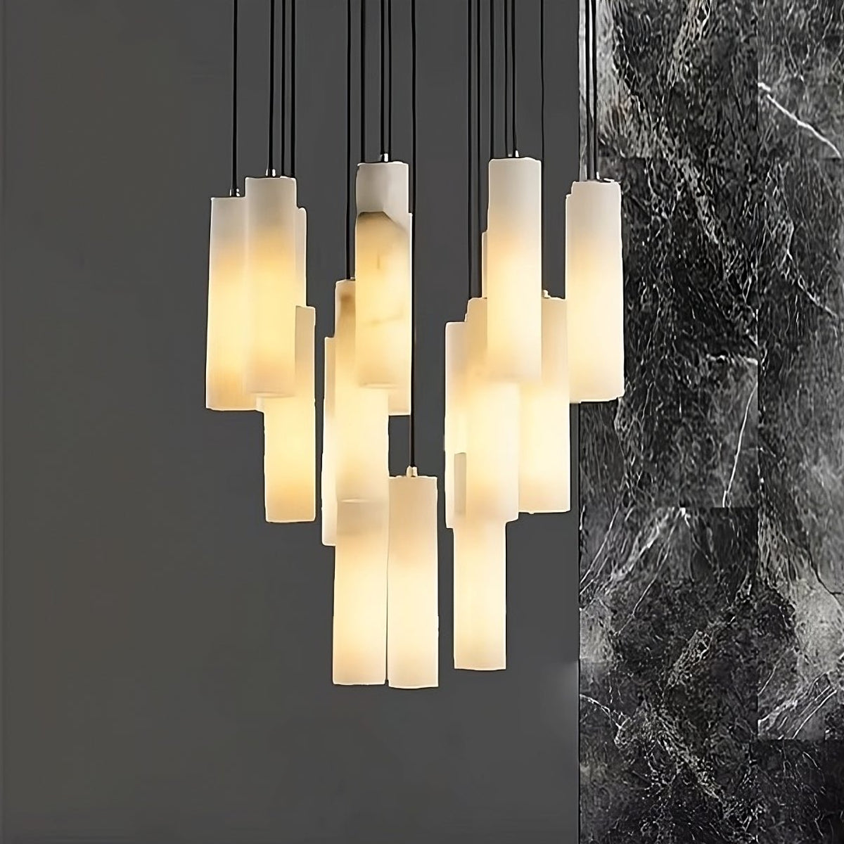 The Moonshade™ Marble Pendant Lighting Fixture by Morsale.com features a modern design with multiple rectangular, frosted glass pendants that emit a warm light. This chandelier creates a striking contrast against a dark grey wall and the textured surface of natural imported marble. The cascading arrangement of pendants is further enhanced by dimmable LED bulbs.