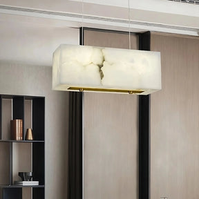 The Natural Marble Dining Room Chandelier by Shopp578 boasts a modern minimalistic design, featuring a translucent alabaster shade. This rectangular pendant light fixture is suspended from a rectangular gold metal plate by two thin wires, offering warm ambient lighting against a plain gray background.