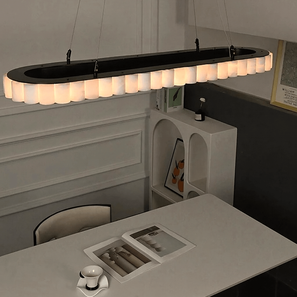 A modern dining room features the Morsale Hampton Marble Dining Room Chandelier with dimmable LED lighting above a white table set with a cup, saucer, and open magazine; minimalist decor and sleek wall shelves complete the look.