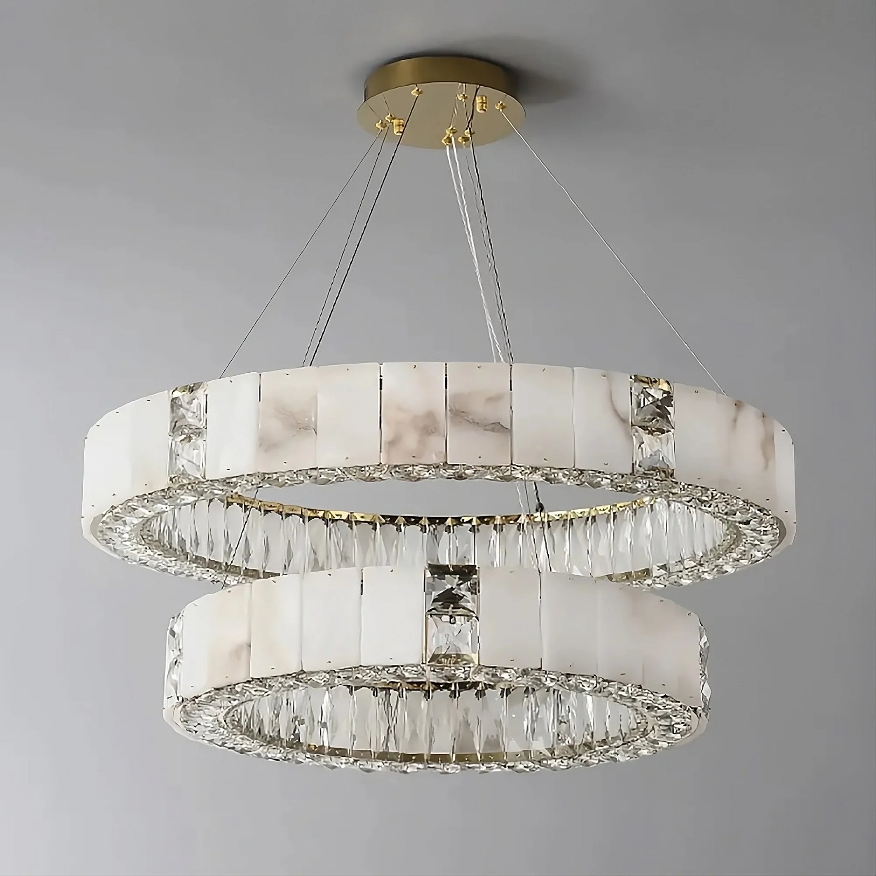 A Natural Marble & Crystal Modern Ceiling Light Fixture from Morsale.com with two circular tiers hangs from a gold base. Each tier is adorned with rectangular translucent panels at the top and a row of crystal-like prisms underneath, creating a luxurious and sophisticated lighting fixture perfect for luxury home décor.
