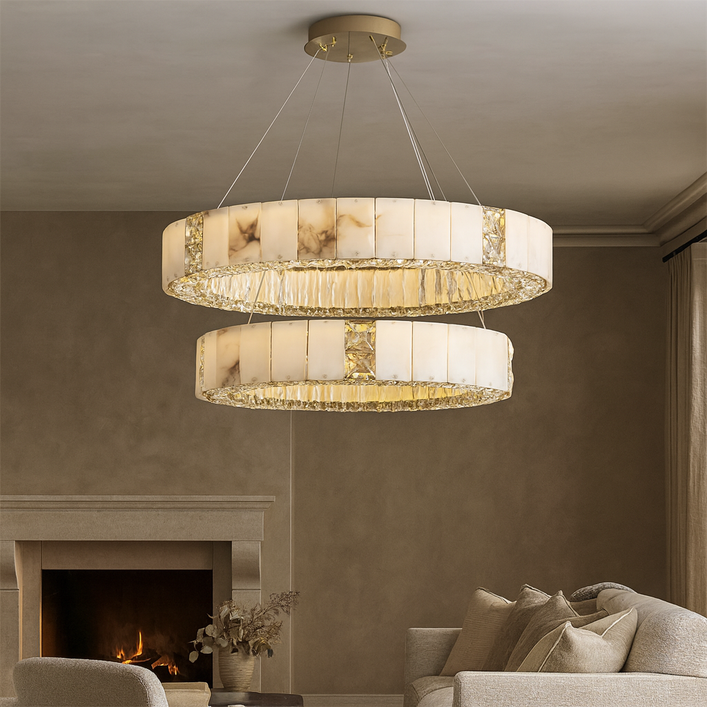 A luxurious living room features the Kolia Stafford Marble & Crystal Chandelier hanging overhead, complemented by a fireplace, light couch, and neutral-toned walls for an elegant, cozy atmosphere.