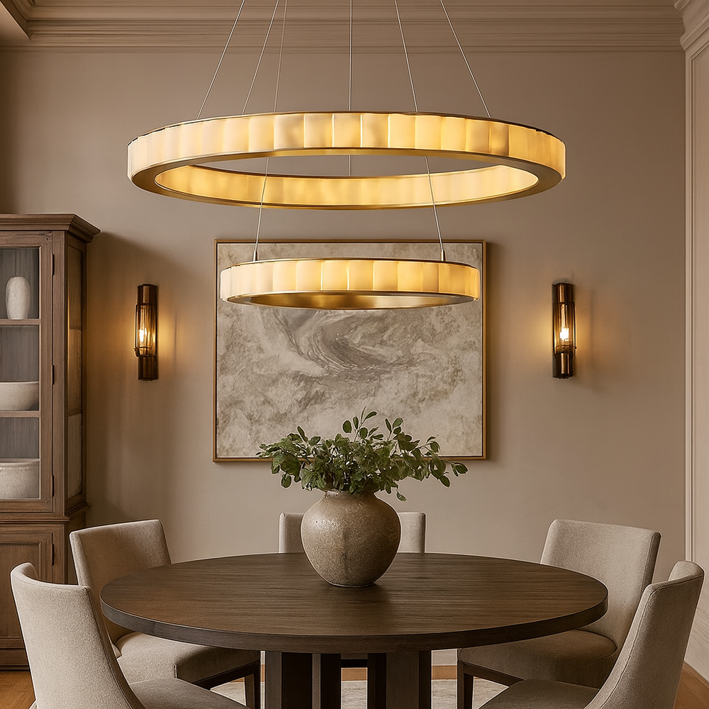 
                  
                    A modern dining room featuring a round wooden table, four beige chairs, a large ceramic vase with greenery, the Bigman Hampton 2-Tier Marble Chandelier overhead, and marble artwork on the wall between two sconces.
                  
                
