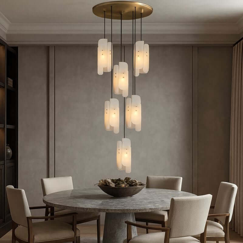 A round dining table with five beige chairs sits beneath Morsale's Lunara Natural Marble & Copper Pendant Lights, adding a modern luxury touch to the neutral-toned dining room with their elegant, dimmable illumination.