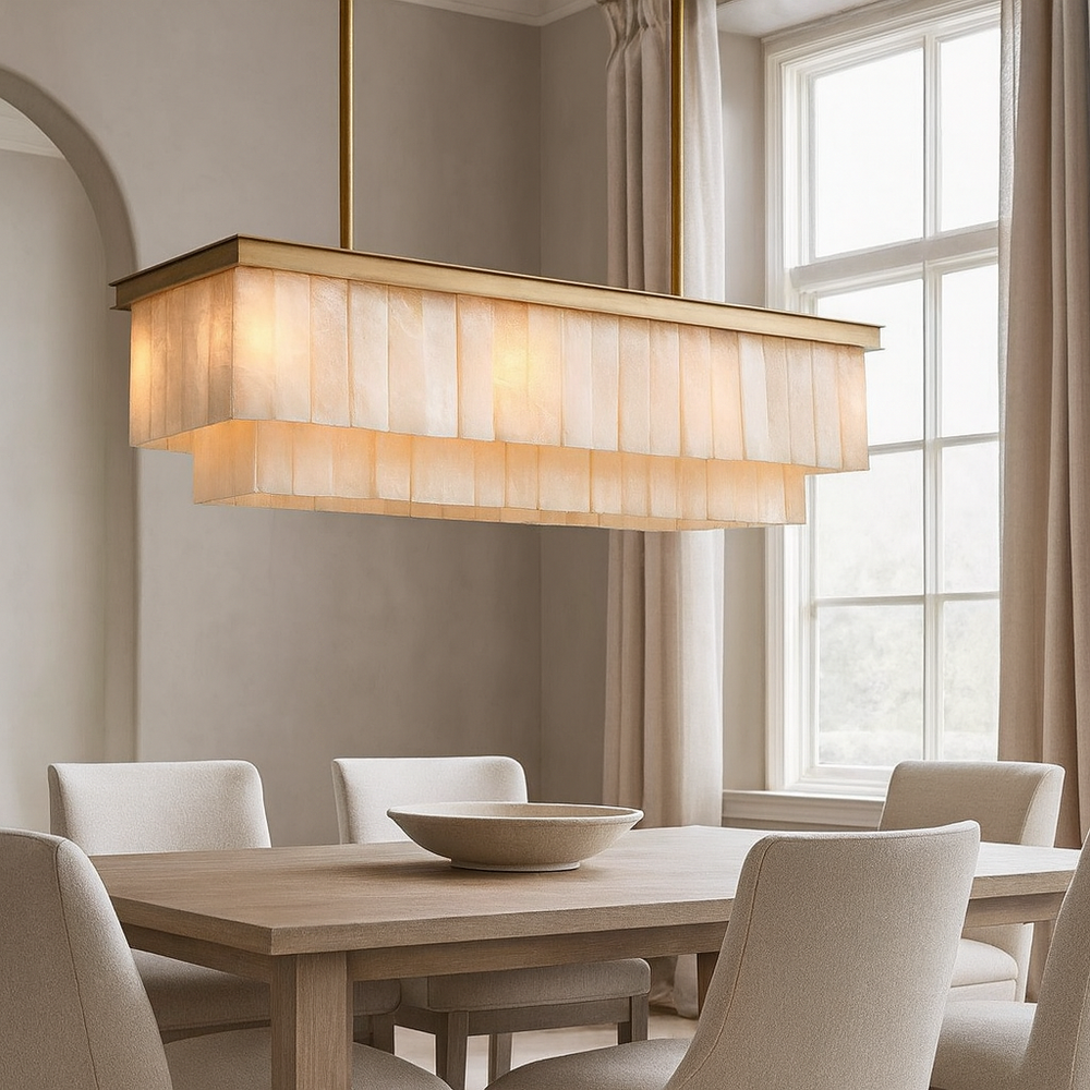 A modern dining room features a rectangular wooden table, four light beige upholstered chairs, a large cream-colored bowl, and the Windsor Marble Dining Chandelier by Shopp578 above, set near tall windows with neutral curtains.
