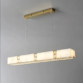 A Natural Marble & Crystal Modern Ceiling Light Fixture by Morsale.com hangs from a ceiling. The fixture has a gold-colored top and supports two wires suspending a long, horizontally oriented light bar consisting of multiple white frosted rectangles with intricate metallic accents, embodying luxury home décor elegance.