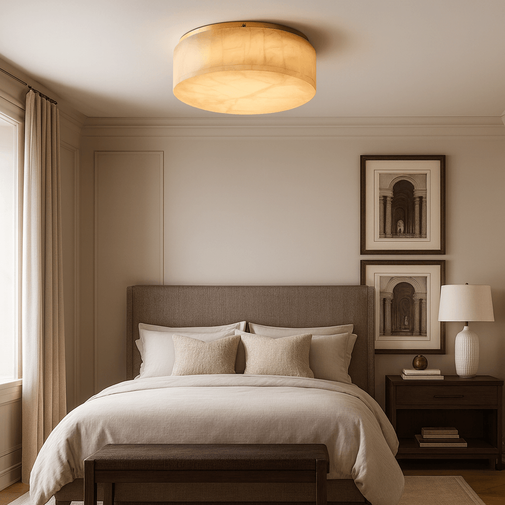 
                  
                    A cozy, neutral-toned bedroom features a beige upholstered bed, cream bedding, two framed wall art pieces, a wooden nightstand with a lamp, and the Milton Marble Flush Mount by Morsale.com overhead. Natural light filters through a curtain.
                  
                