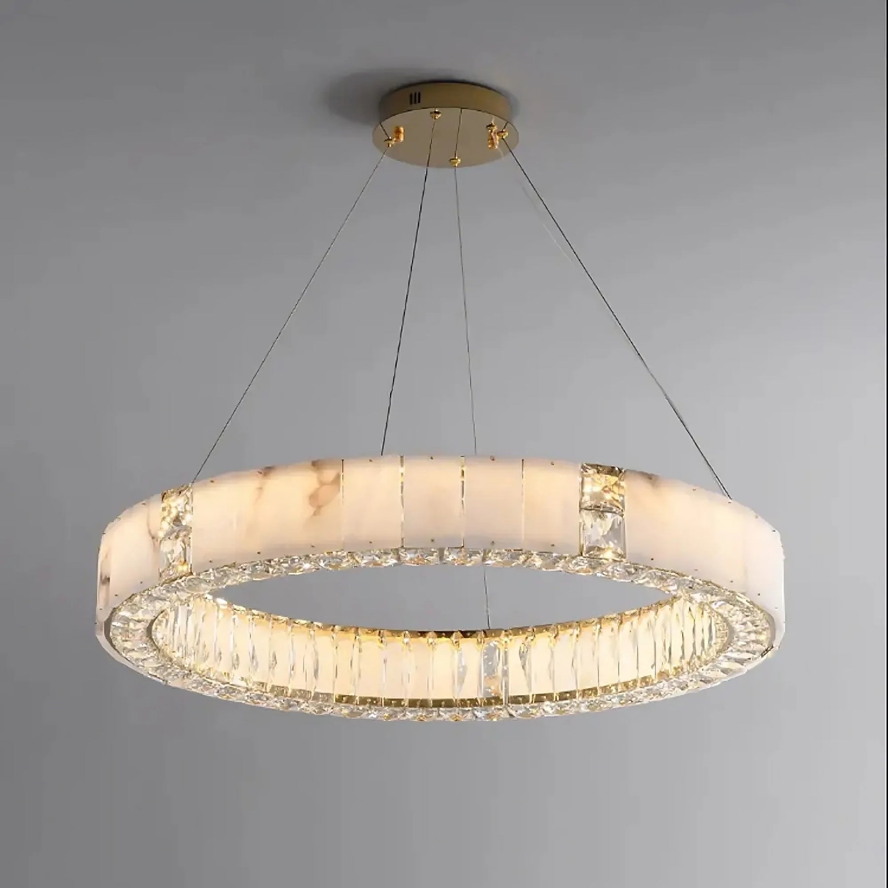 A Morsale.com Natural Marble & Crystal Modern Ceiling Light Fixture with a gold-toned frame, suspended by thin wires. This luxury home décor piece features a band of translucent, natural marble-like material and is adorned with crystals around the inner and outer edges, casting an elegant light.