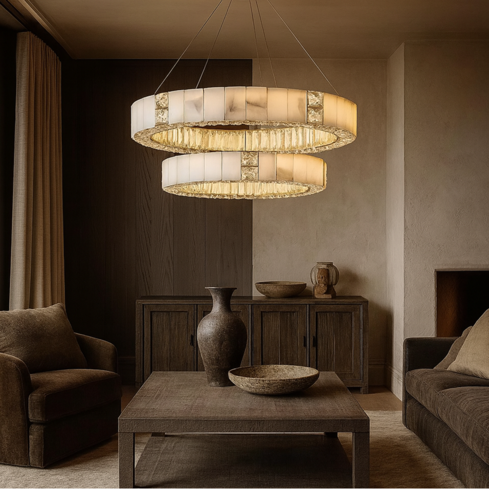 A cozy living room featuring the Kolia Stafford Marble & Crystal Chandelier, brown sofas, a wooden coffee table with decorative bowls, a tall vase, and dark wood cabinets set against neutral-colored walls.
