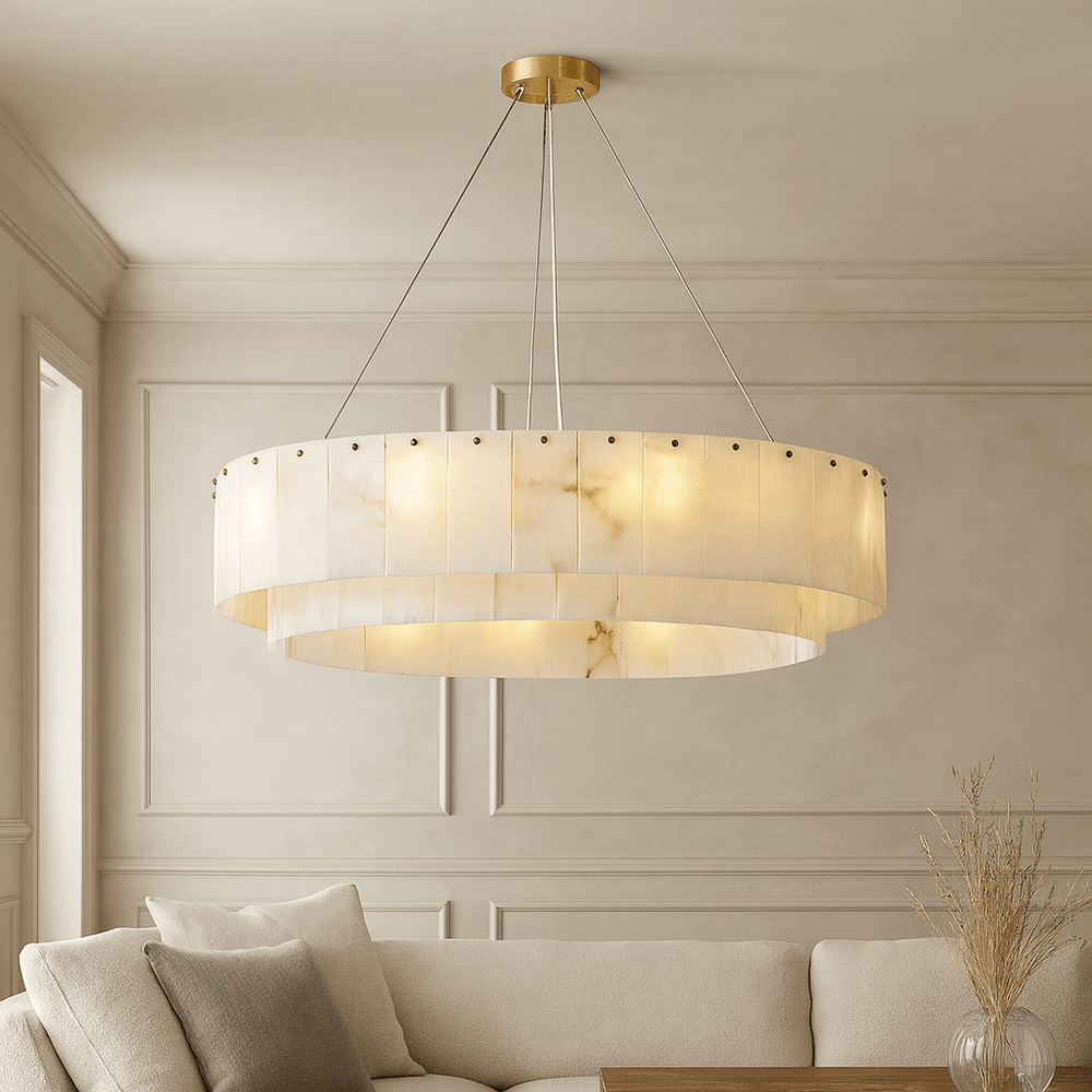 
                  
                    The Buckley Marble Modern Chandelier by Bigman, featuring a warm alabaster shade, hangs in an elegant neutral-toned living room with a sofa, wooden table, and decorative dried grass in a vase.
                  
                