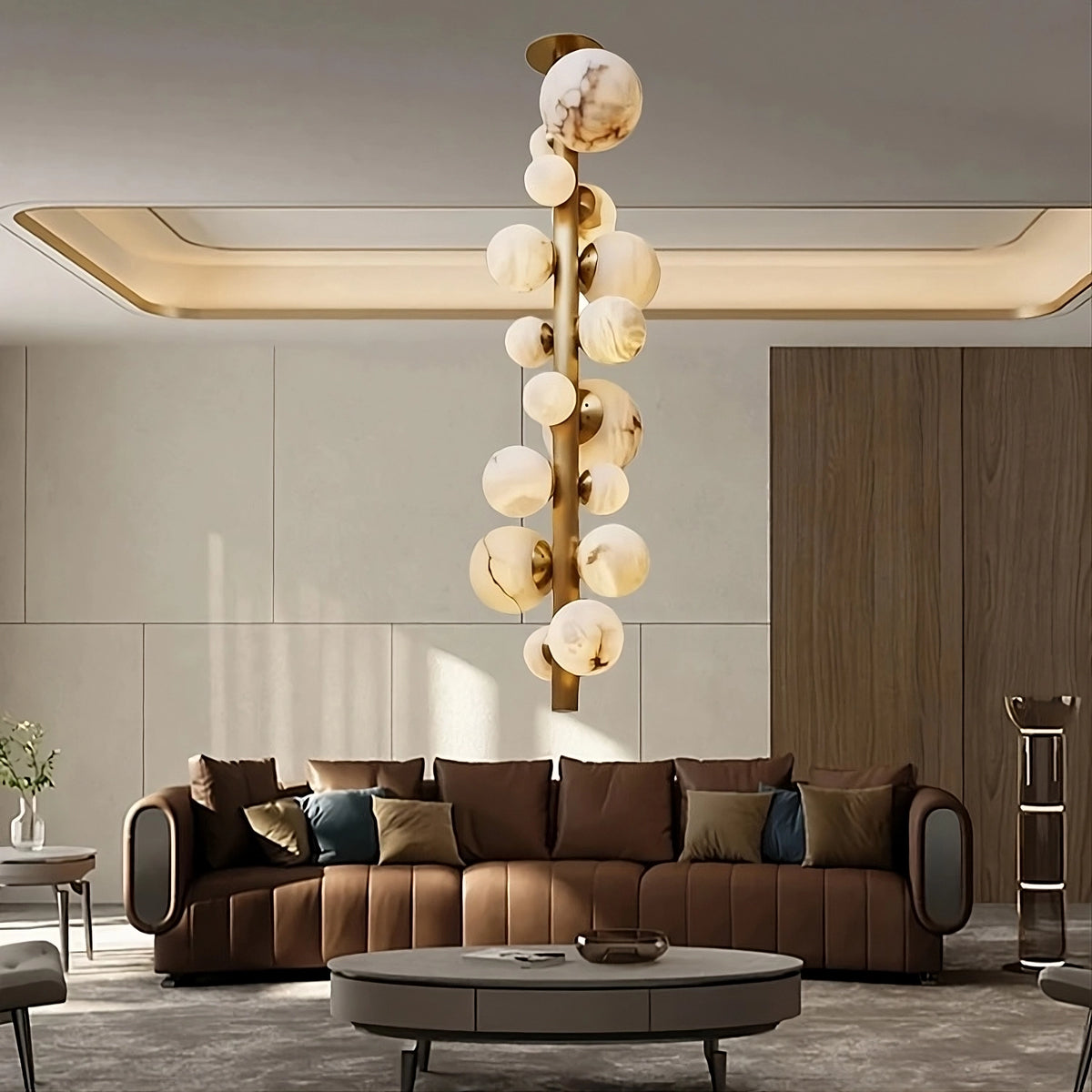 A modern living room features a brown leather sofa with assorted pillows, a round coffee table, and the distinctive Moonshade Luxury Marble Ball Chandelier by Morsale, featuring copper accents and spherical elements. The room is illuminated by energy-efficient LED bulbs and has neutral walls paired with a wooden panel accent.