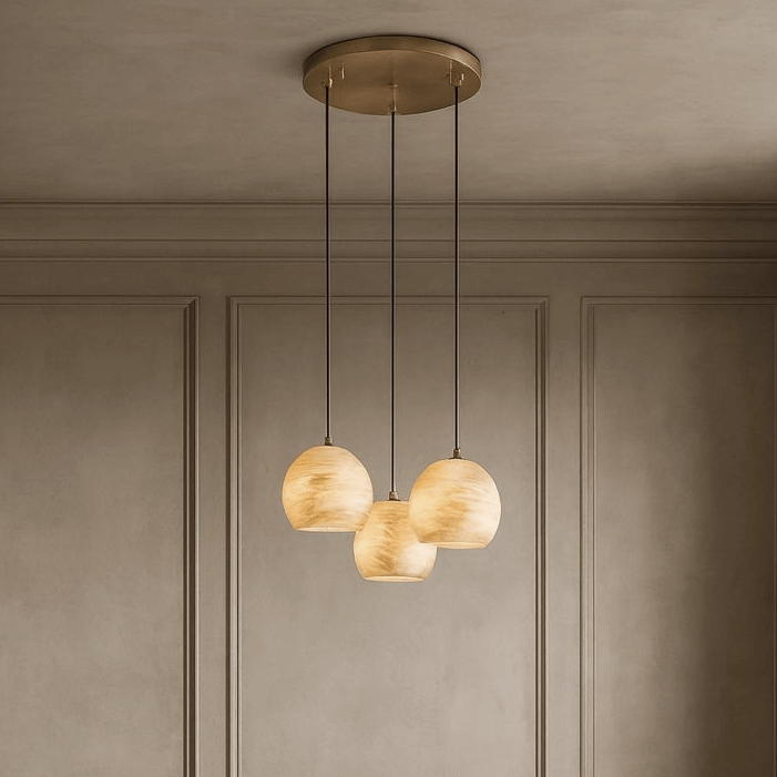 The Auris 3-Light Marble Chandelier by Morsale.com features three cream glass globes hanging at varied heights from a brass mount, creating ambient lighting ideal for contemporary spaces with beige paneled walls.