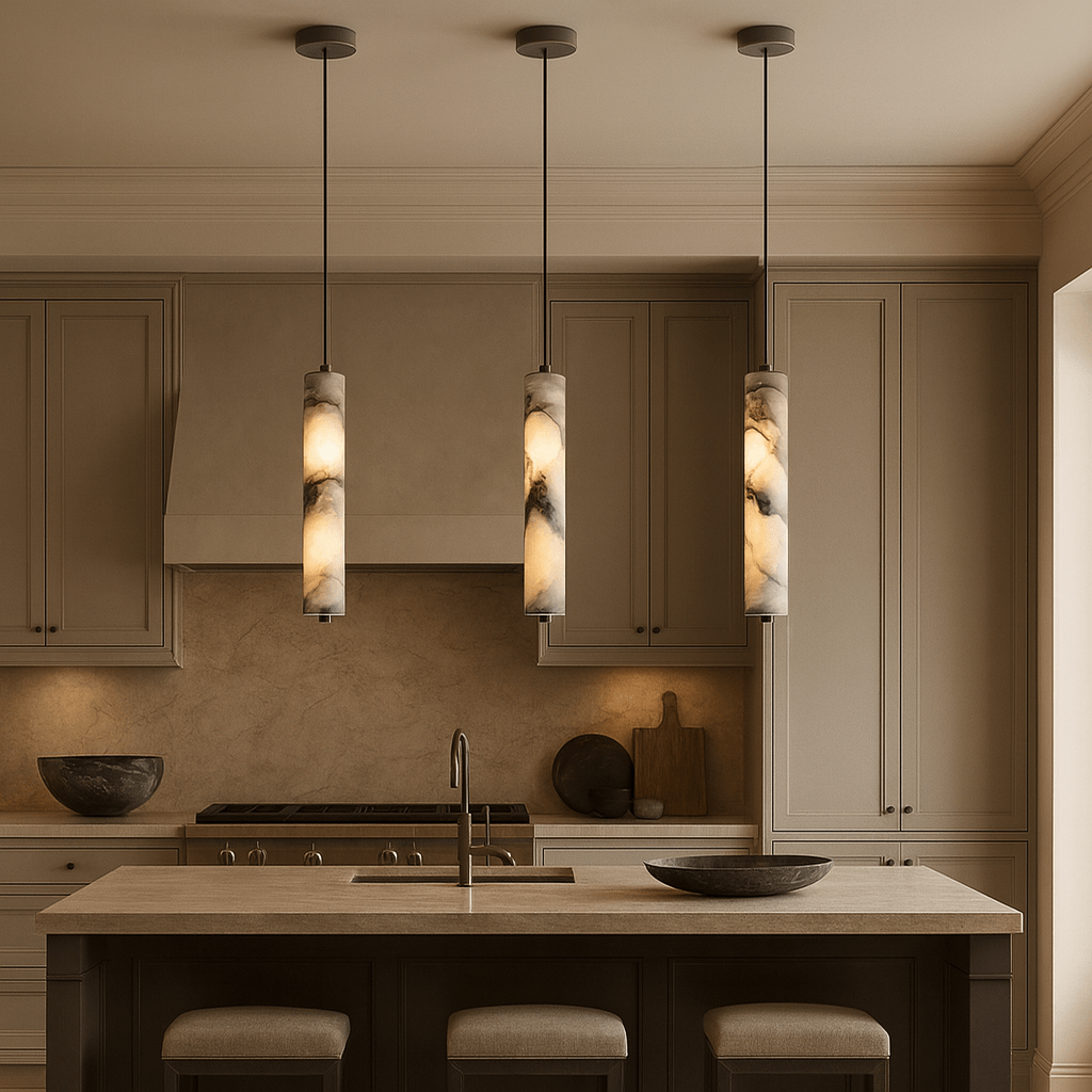 A modern kitchen with beige cabinets, a central island with a sink, three Morsale Valmont Marble Cylinder Pendant Lights overhead, two cushioned stools, and counters with decorative bowls and cutting boards accented by modern LED lighting.