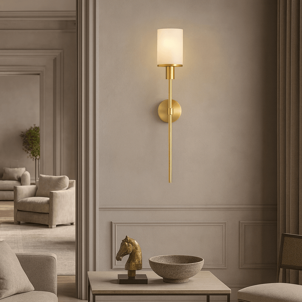 The Caldera Marble & Copper Wall Sconce by Morsale, featuring a cylindrical white shade, is mounted above a console table displaying a gold horse head and round marble bowl. Neutral-toned furniture appears in the background.