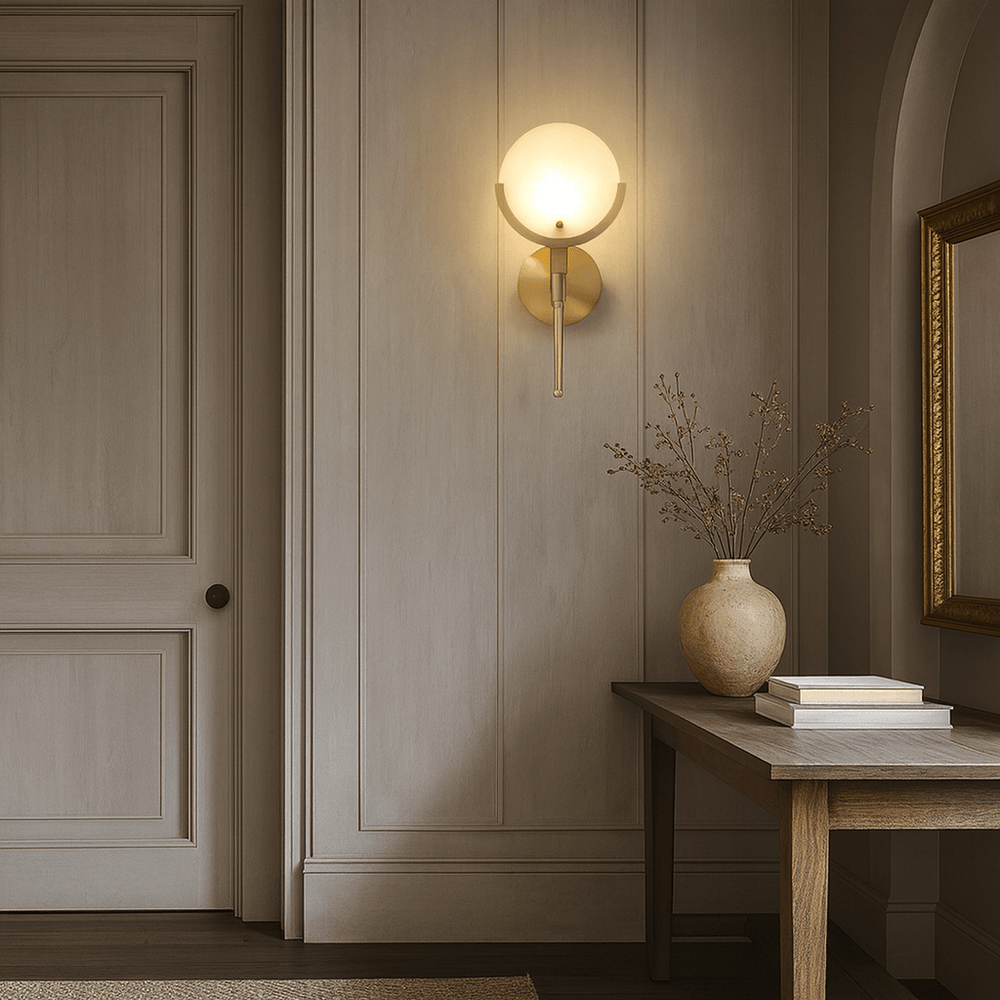 
                  
                    A softly lit hallway features beige paneled walls, the Vellaro Marble Wall Sconce from Morsale.com for luxurious lighting, a wooden console table with a ceramic vase of dried branches, two stacked books, and a framed mirror.
                  
                