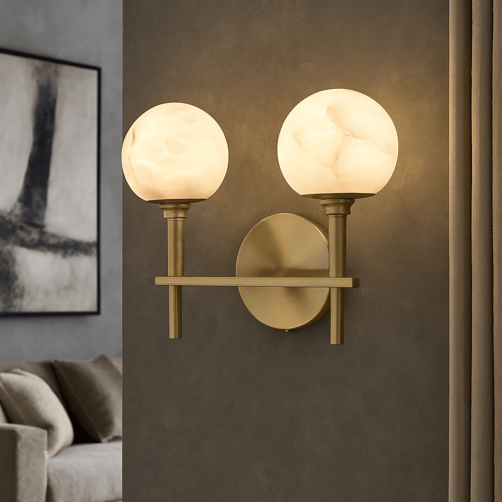 The Morsale Aria Copper & Marble Wall Sconce features two round frosted glass globes, emitting soft light. Mounted on a gray wall near beige curtains, it adds modern style to any contemporary living room.