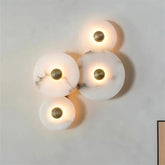 A wall-mounted Moonshade Natural Marble Wall Sconce from Morsale.com features four circular, handmade sconces with marble-like glass panels and central brass accents, emitting soft, warm light against a smooth, light-colored wall. This lighting arrangement forms a visually appealing cluster.