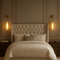 A cozy, elegant bedroom features a tufted beige headboard, neutral bedding, dark wood nightstands, and two Moonshade Marble Pendant Wall Sconces by Morsale.com on paneled walls—perfect for refined home decor.