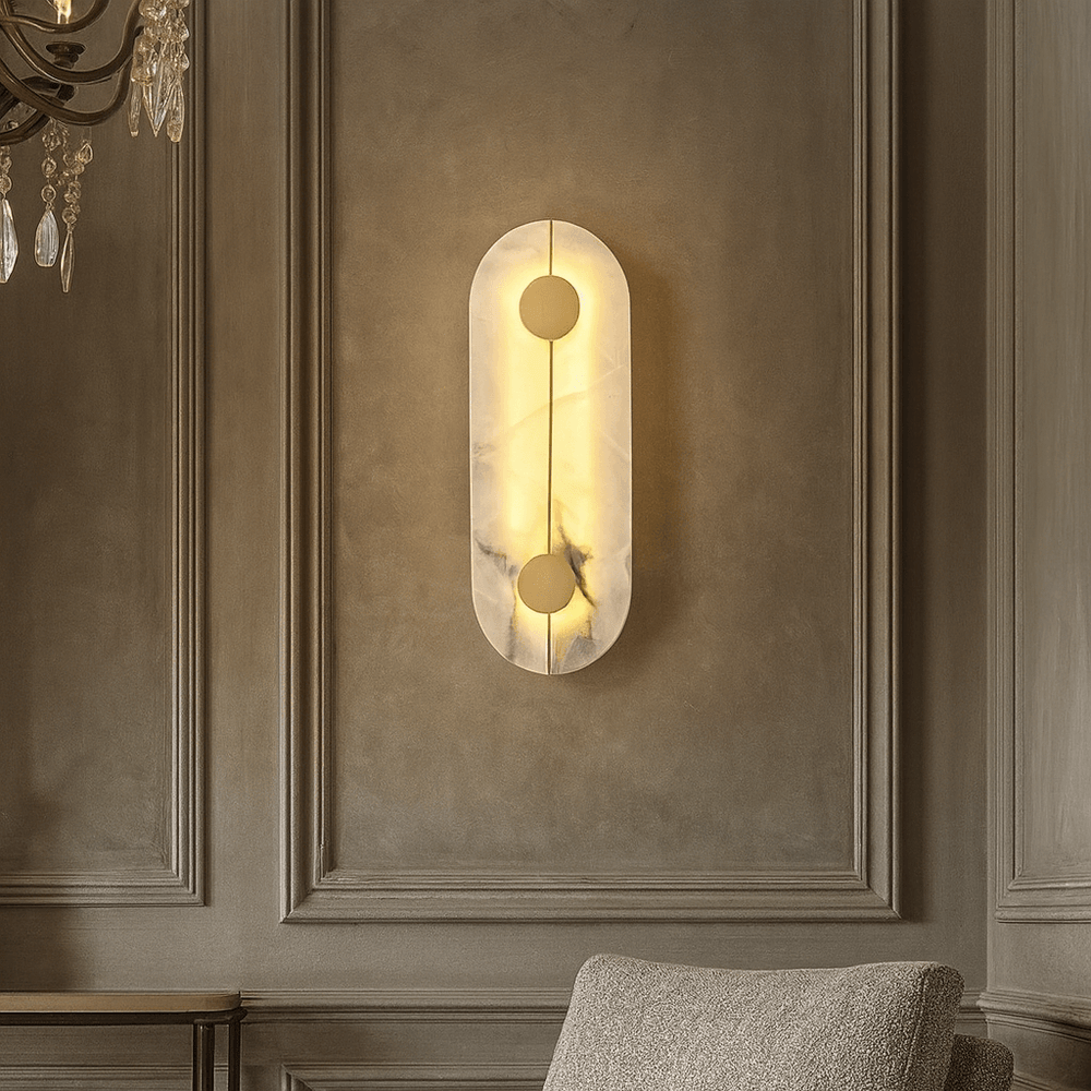 The Haddon Marble Sconce by Morsale.com features an oblong design and a soft, warm glow, elegantly mounted above a textured beige armchair on a paneled wall.