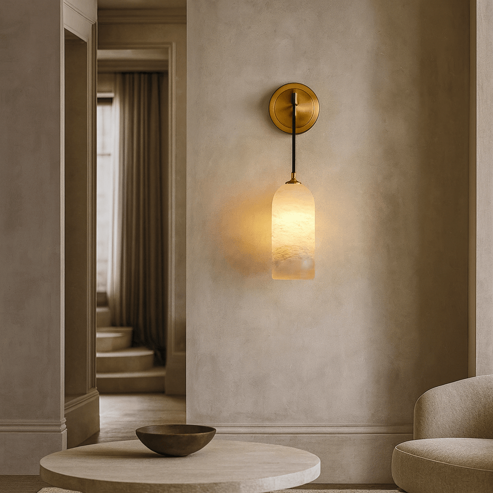 The Lucera Marble Pendant Sconce by Morsale, featuring a brass fixture and frosted glass shade, is mounted on a beige wall in a modern, minimalist living room with neutral furniture and a decorative bowl on a circular table.